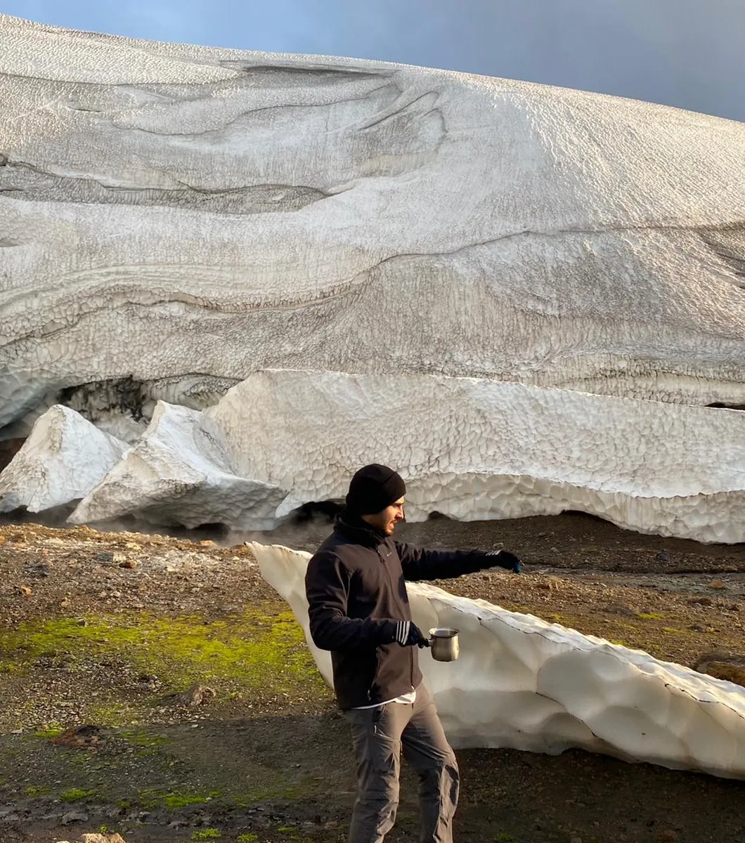 Nir holding a camping mug in front of a glacier ice cave in Iceland